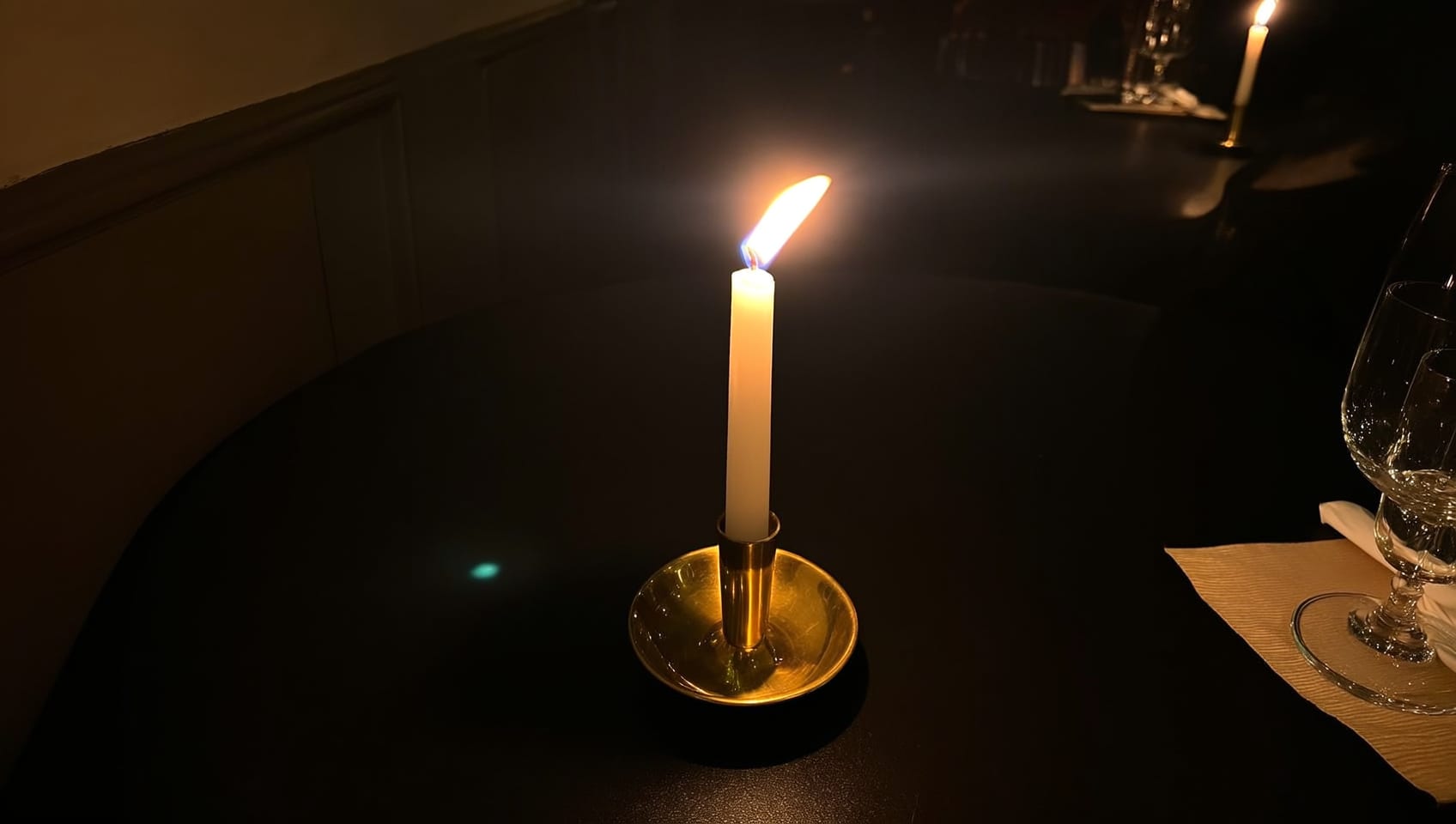 A single lit taper candle in a brass holder on a dark table at night