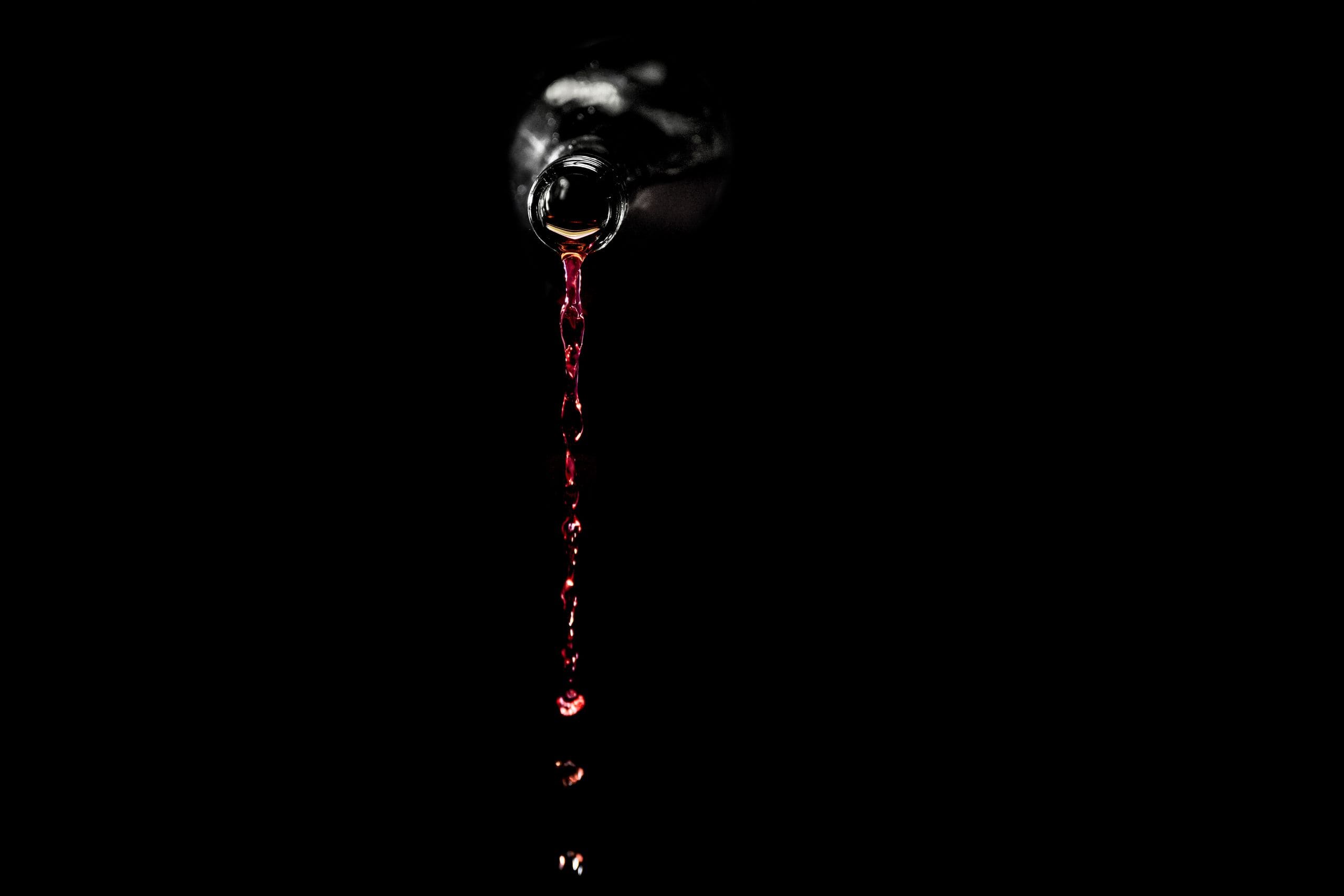 Wine poured into a crystal glass against total darkness, the only light in the frame